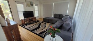 A living room with a sofa, a television, a coffee table with a plant, and a patterned rug. - Recovery On Discovery Holiday House (Agnes Water)