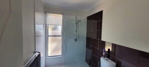 A modern bathroom with a glass shower enclosure, a white toilet, and a dark tiled wall. - Recovery On Discovery Holiday House (Agnes Water)