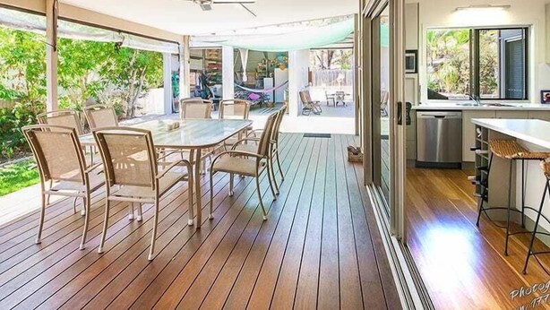 A modern kitchen with a large island, a dining area with a table and chairs, and a view of the outdoors. - Recovery On Discovery Holiday House (Agnes Water)