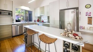A modern kitchen with white cabinets, stainless steel appliances, and a large island with bar stools. - Recovery On Discovery Holiday House (Agnes Water)