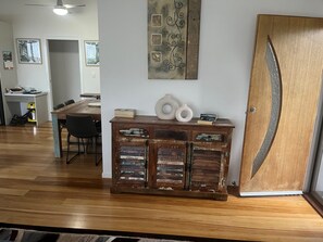 A dining area with a wooden table and chairs, a decorative cabinet with books and vases, and a door with a unique design. - Recovery On Discovery Holiday House (Agnes Water)
