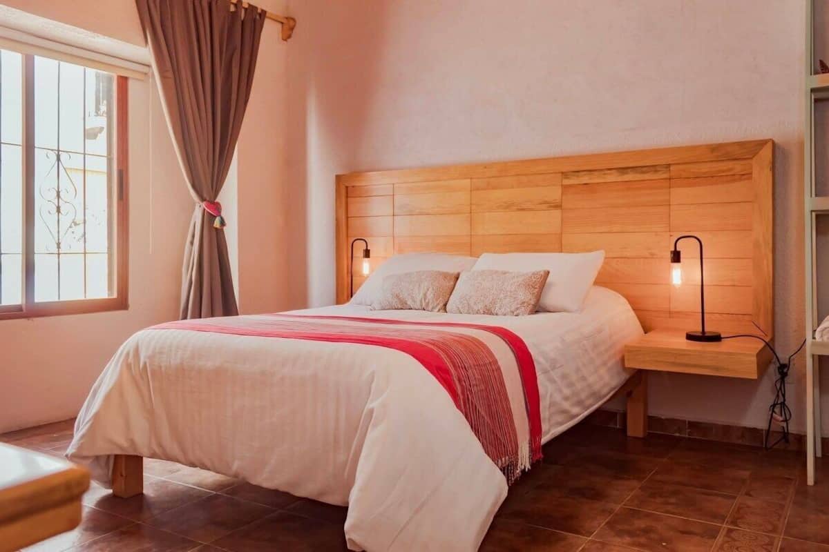 Ein ordentlich bezogenes Bett mit Holz Kopfteil, zwei Nachttischlampen und einer roten und weißen Tagesdecke.