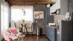 Een kleine keuken met een koelkast, magnetron en een eethoekje met een tafel en stoelen.