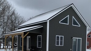 Uma casa de dois andares com varanda coberta e mesa de piquenique na neve.