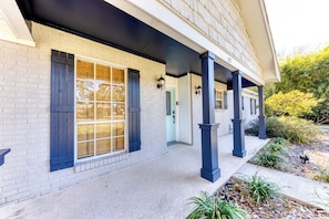 A two-story house with a covered porch, white brick exterior, and dark shutters. - POOL with Heating option! 6-seater Golf Cart &GameRoom! Walk to Beach &Downtown! (Long Beach)