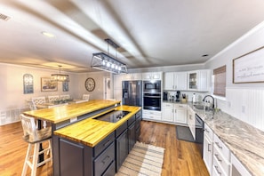 A modern kitchen with a wooden island, stainless steel appliances, white cabinetry, and a decorative wall clock. - POOL with Heating option! 6-seater Golf Cart &GameRoom! Walk to Beach &Downtown! (Long Beach)