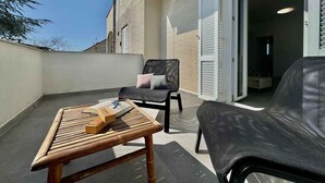 Un balcón al aire libre con una mesa de madera, dos sillas y una puerta que da a un espacio interior.