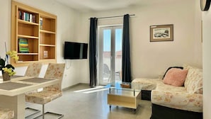 Una sala de estar con sofá, una mesa de centro, televisor montado en la pared, estantería y puerta de cristal que da al exterior.