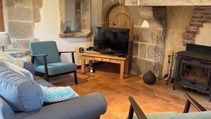 A cozy living room with a stone fireplace, a television on a wooden stand, and comfortable seating.