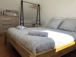 Une chambre à coucher avec un cadre de lit en bois, du linge de lit blanc, une table de chevet avec une lampe et un étendoir fixé au mur.