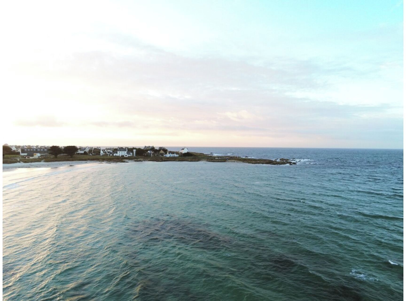 A coastal view with a calm sea, a small settlement with houses, and a clear sky.