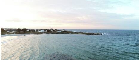 A coastal view with a calm sea, a small settlement with houses, and a clear sky.
