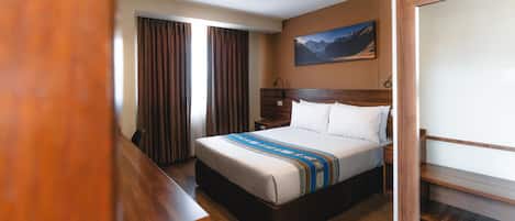 Habitación de hotel con cama, suelo de madera, cortinas, un cuadro en la pared y un escritorio.