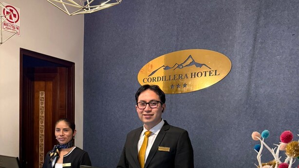 Een hotel receptiebalie met een bord waarop 'CORDILLERA HOTEL' staat en een decoratieve boomsculptuur.