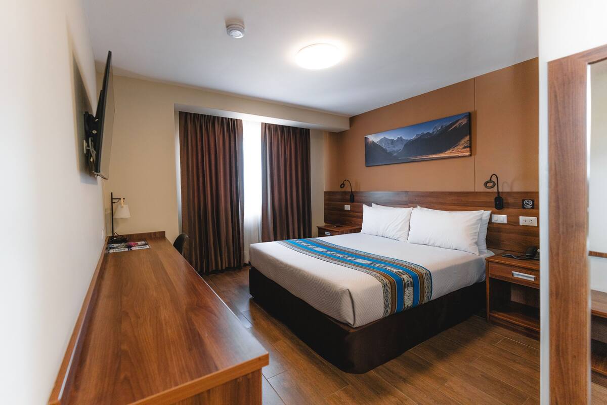 A hotel room with a large bed, wooden bench, and a painting on the wall.