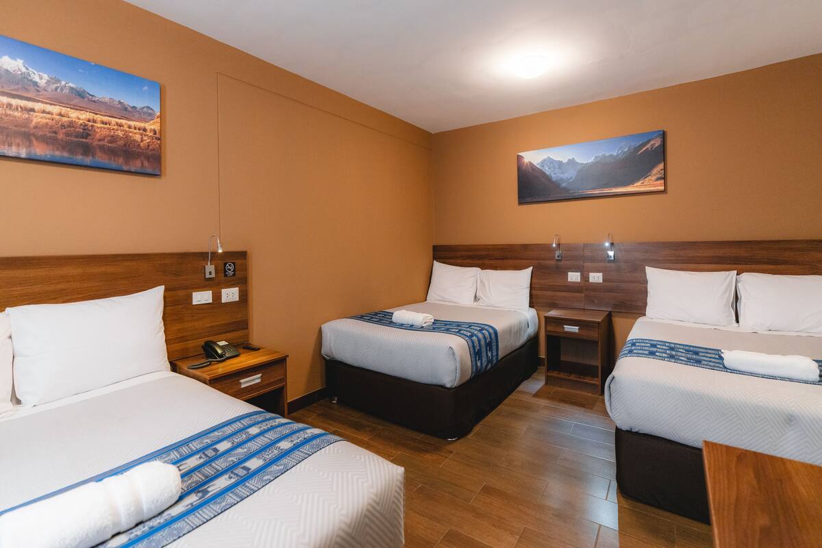 A hotel room with two beds, wooden headboards, a nightstand with a phone, and a painting on the wall.