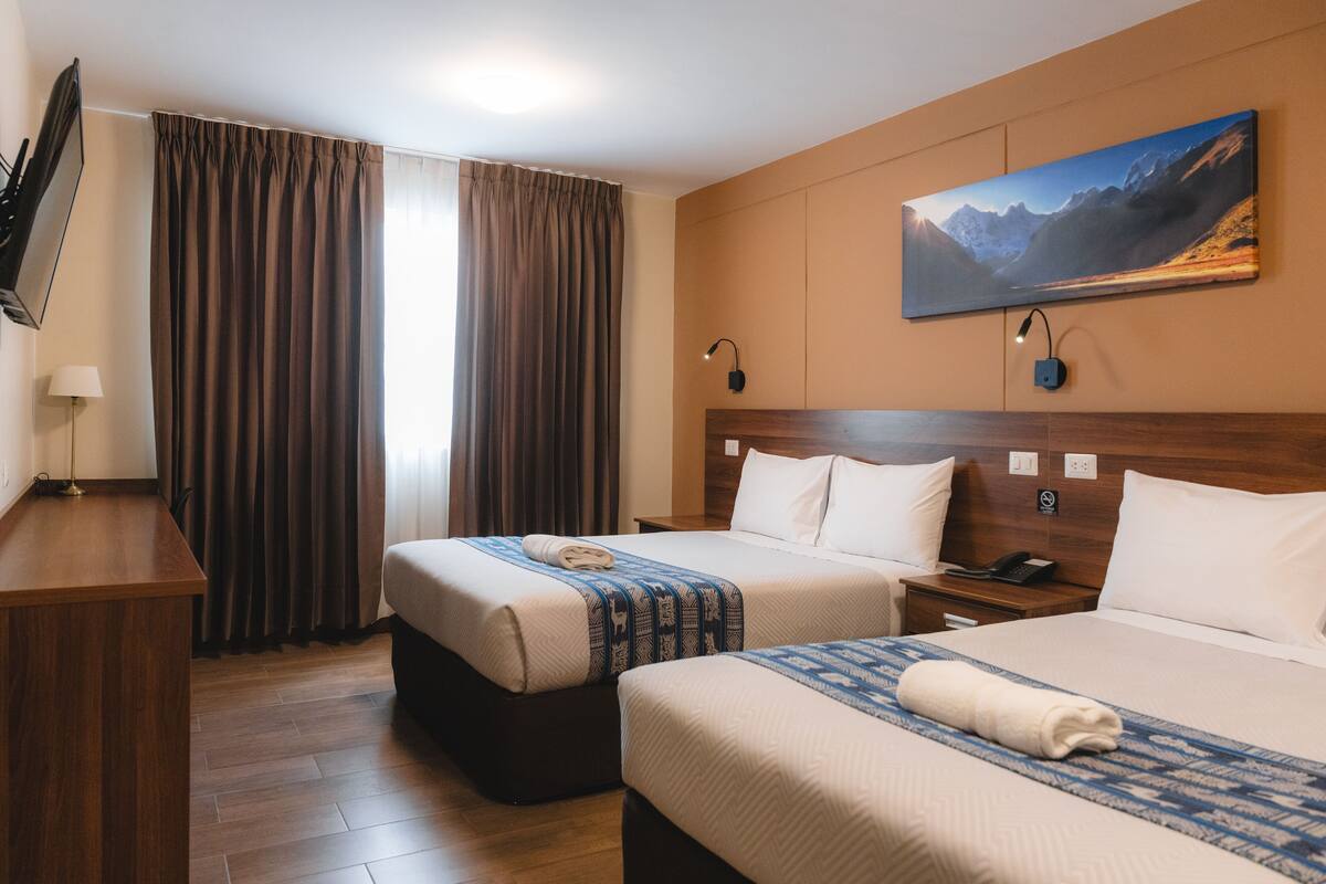 A hotel room with two beds, a desk, a TV, and a painting on the wall.