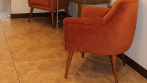 Een hal met twee oranje stoelen, een houten tafel, een schilderij en een lift.
