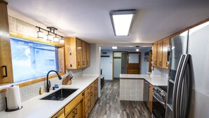 A modern kitchen with wooden cabinets, a stainless steel refrigerator, and a large window.