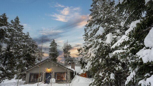 A log cabin with a porch, surrounded by snow-covered trees.