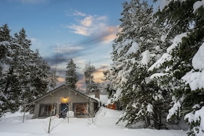 A log cabin with a porch, surrounded by snow-covered trees.