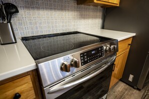 A kitchen with a stainless steel stove, a white countertop, wooden cabinets, and a patterned backsplash.