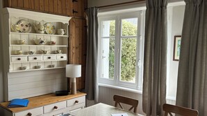 En matplats med ett träskåp, ett bord med ett vitt bordsduks, stolar, en lampa och ett fönster med gardiner.