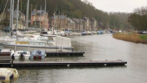 En småbåtshamn med olika typer av båtar förtöjda längs en flodbank, omgiven av bostadshus.