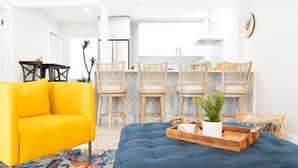 A bright yellow sofa, a blue ottoman, and a patterned rug in a modern living room. - Modern Oasis (Oakland Park)