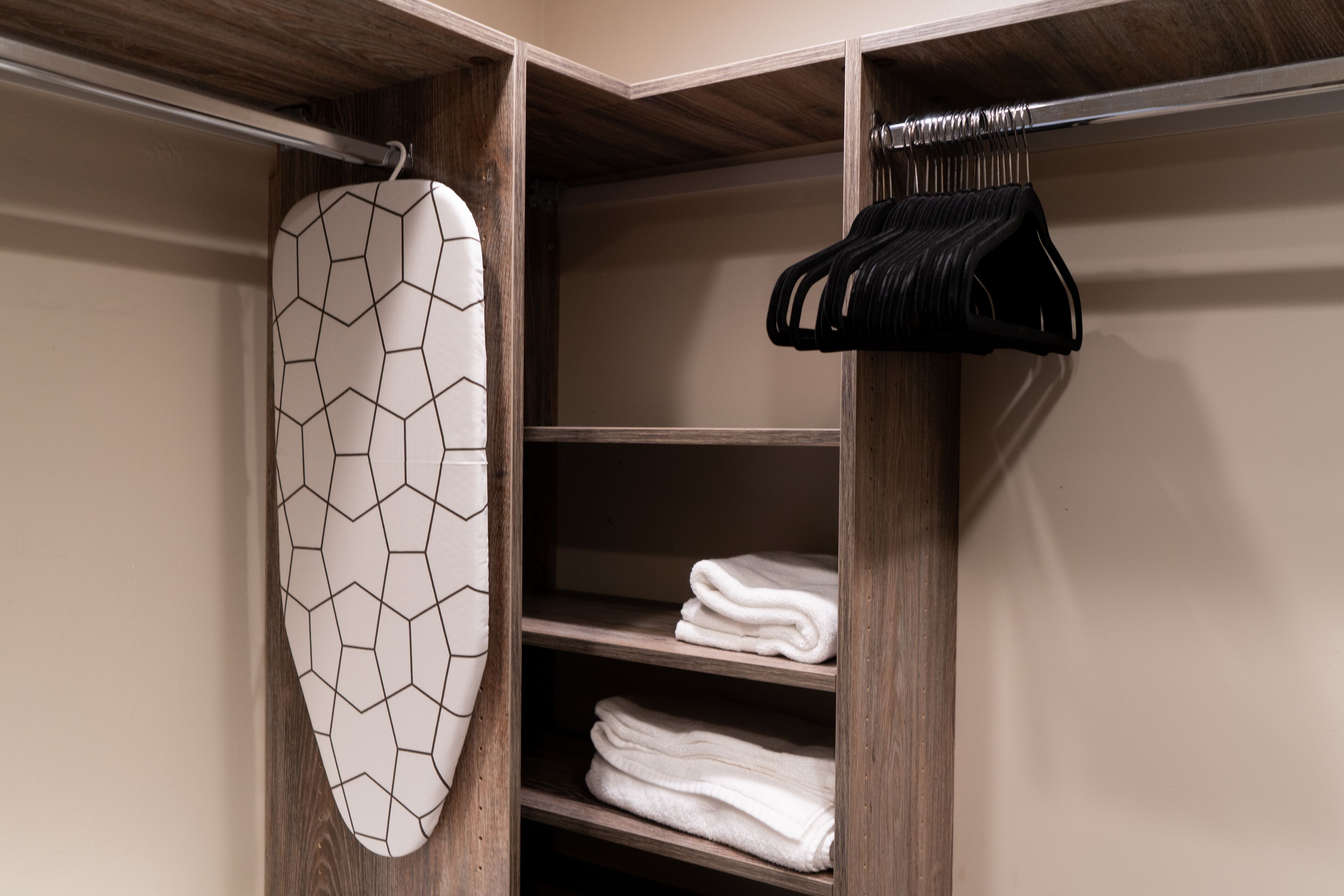A closet with wooden shelves, a hanging rack, and an ironing board.