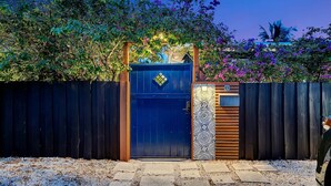 A gated entrance with a blue door, a wooden fence, and a decorative wall with a patterned design. - Modern Oasis (Oakland Park)