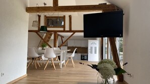 Ein modernes Interieur mit Essbereich, Holzbalken, einem Flachbildfernseher und einer Küche im Hintergrund.