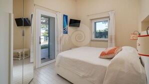 Ein Schlafzimmer mit Bett, Fernseher, Fenster und einer Tür, die auf einen Balkon führt.