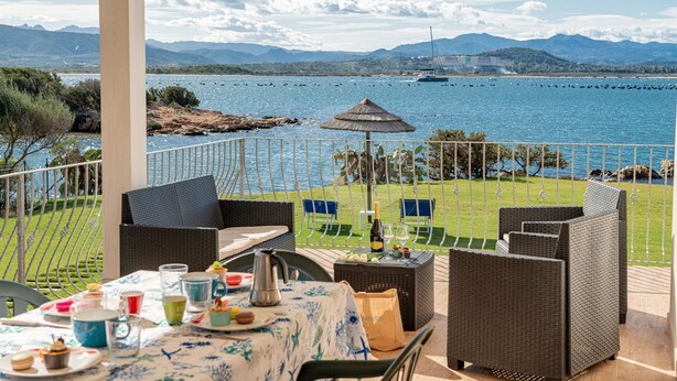 Eine Terrasse mit Korbmöbeln, einem für eine Mahlzeit gedeckten Tisch und Blick auf das Meer und die Berge.