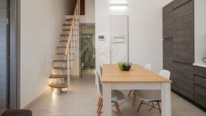 Eine moderne Küche mit Holztisch und -stühlen, einer Treppe und einer weißen Wand mit einer Lampe.