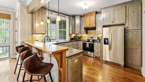Una cucina moderna con mobili in legno, un frigorifero in acciaio inossidabile e un angolo bar con sgabelli.