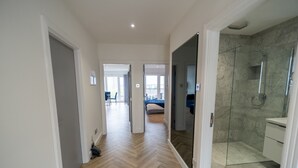 A hallway leading to a bedroom with a bed, a bathroom with a glass shower, and a dining area with chairs and a table. - Stunning Penthouse - Birmingham City Centre (Birmingham)