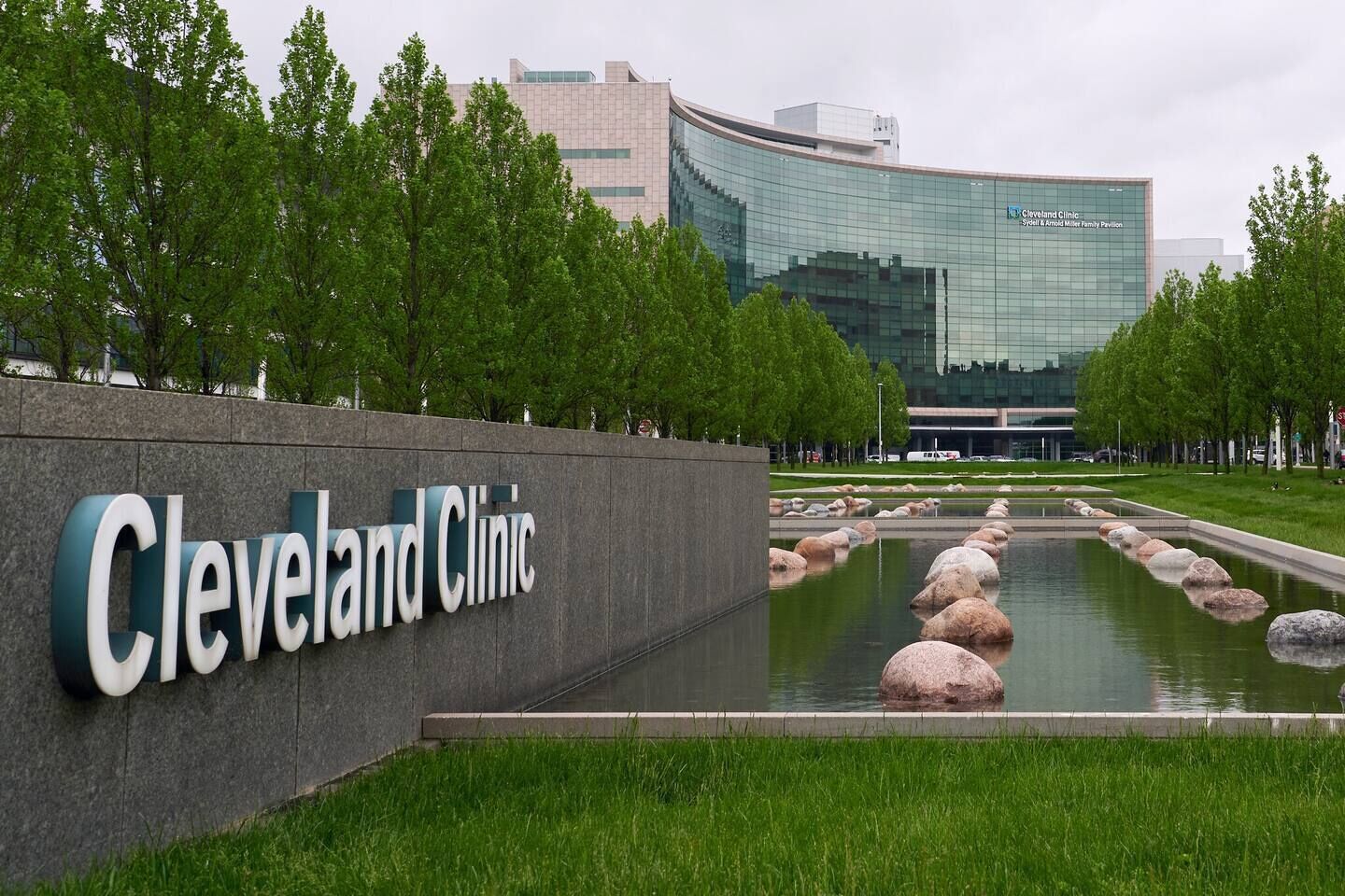 Een bord van Cleveland Clinic met een modern gebouw op de achtergrond en een waterpartij met stenen.