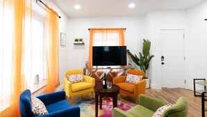 Un salon équipé d’un téléviseur à écran plat, de deux fauteuils jaunes, d’un fauteuil bleu et d’un fauteuil vert.