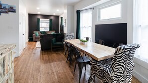 Una sala moderna con una mesa de comedor de madera, sillas con estampado de cebra, un sofá y un sillón verde.