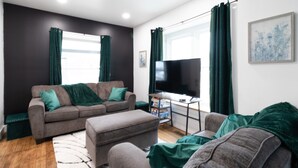 A living room with a grey sofa set, a flat-screen TV, and a small table with a remote control. - Spacious 8 BR Near CWRU, Cleveland Clinic, & UH! (Cleveland)