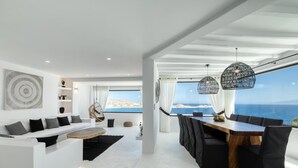 Una sala moderna con una gran mesa de comedor de madera, sillas negras, un sofá blanco y vistas al mar.