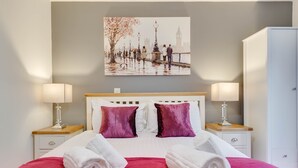 Ein ordentlich bezogenes Bett mit zwei Kissen, zwei Nachttischen inklusive Lampen, einem Kleiderschrank und einem Wandbild, das eine Brücke zeigt.