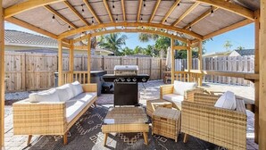 Una veranda esterna coperta con mobili in vimini, un barbecue e un tappeto decorato.