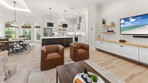 Un vaste espace de vie comprenant un grand téléviseur, une table à manger et deux fauteuils marron.
