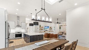 Une cuisine moderne avec des meubles blancs, un îlot central et un coin repas comprenant une table et des chaises en bois.