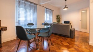 Een moderne woonkamer met een ronde glazen tafel, vier stoelen, een bank en een televisie.