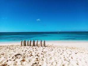 A beach with clear blue water and a row of metal structures on the sand. - Few steps from the ocean, Two bedrooms apartment-CORAL GARDENS-Grand Turk Island (Turks Islands)