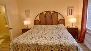 A bedroom with a floral bedspread, two bedside lamps, a wooden headboard, and a small decorative mirror on the wall. - Few steps from the ocean, Two bedrooms apartment-CORAL GARDENS-Grand Turk Island (Turks Islands)