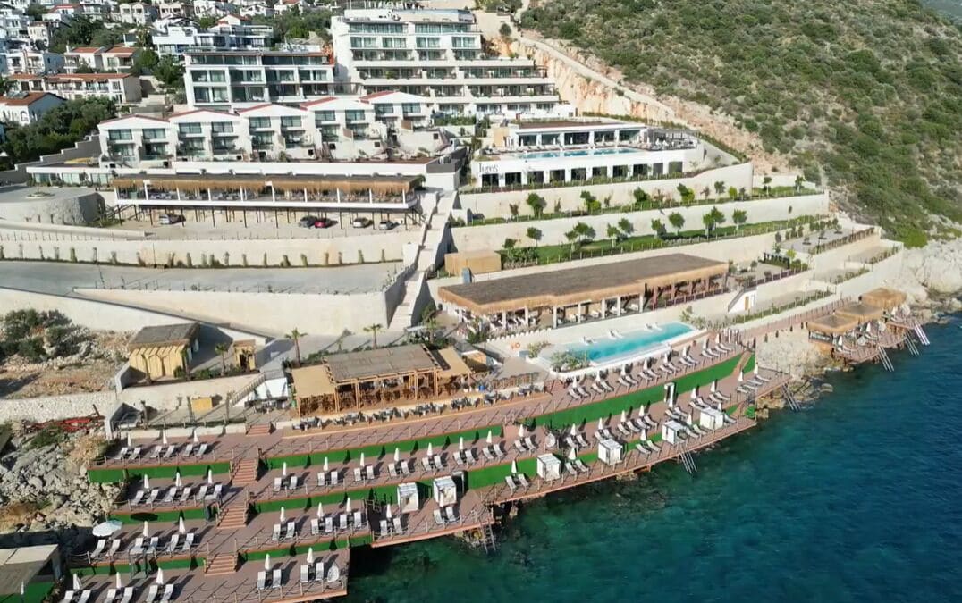 Vista aérea de un hotel costero con varias edificaciones, una zona de piscina y un muelle con tumbonas.